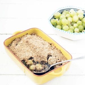 gooseberry crumble in yellow dish with bowl of gooseberries in background
