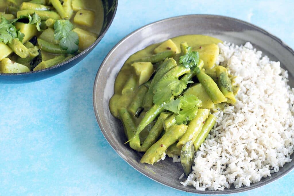 coconut green bean curry on ceramic plate with rice and black saucepan in background