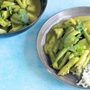 coconut green bean curry on ceramic plate with rice and black saucepan in background