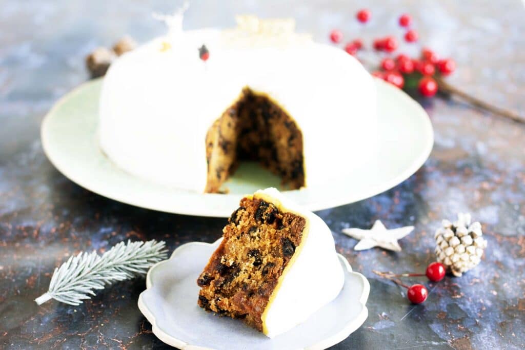 iced vegan Christmas cake with slice on blue plate in foreground