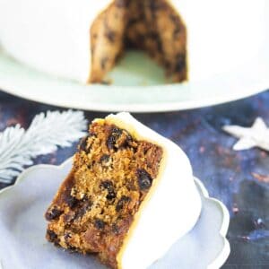 iced vegan Christmas cake with slice on blue plate in foreground