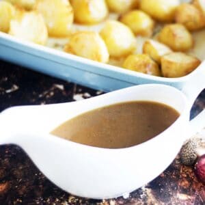 vegan gravy in white gravy boat with roast potatoes and Christmas table decorations