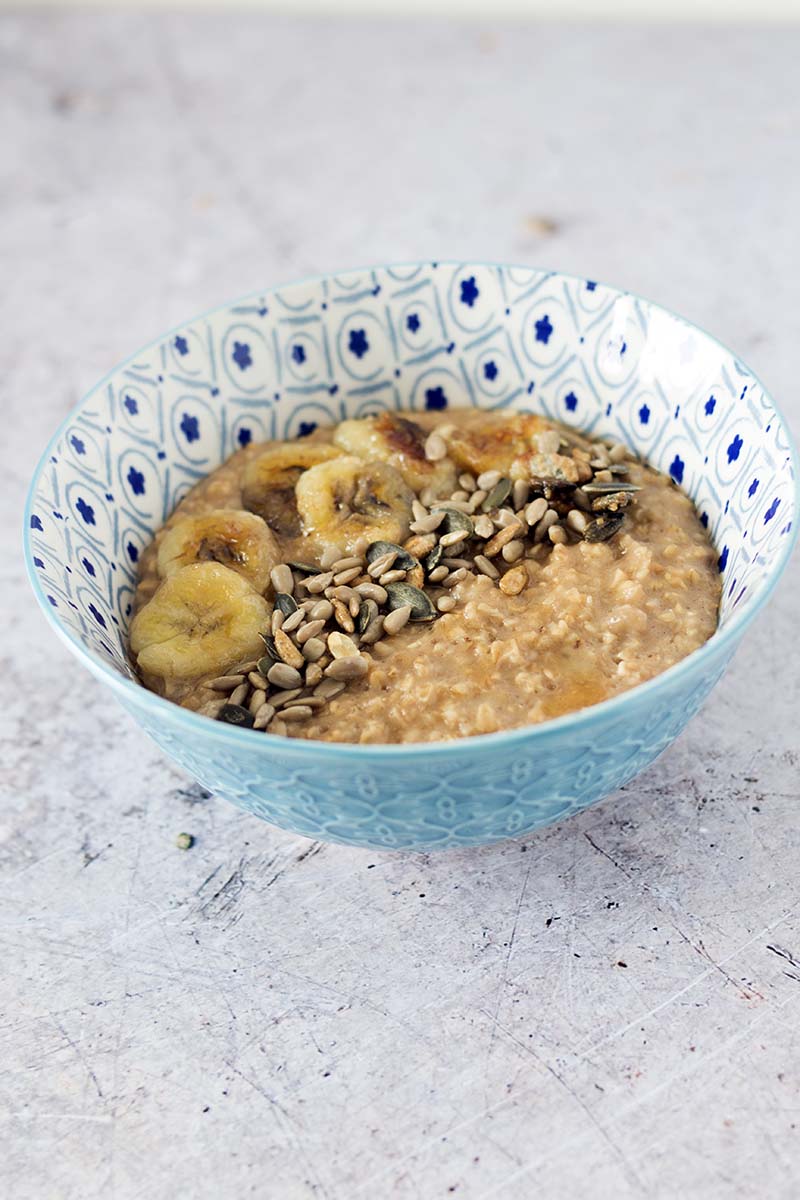 banana oatmeal in blue bowl with sliced banana, seeds and maple syrup on top