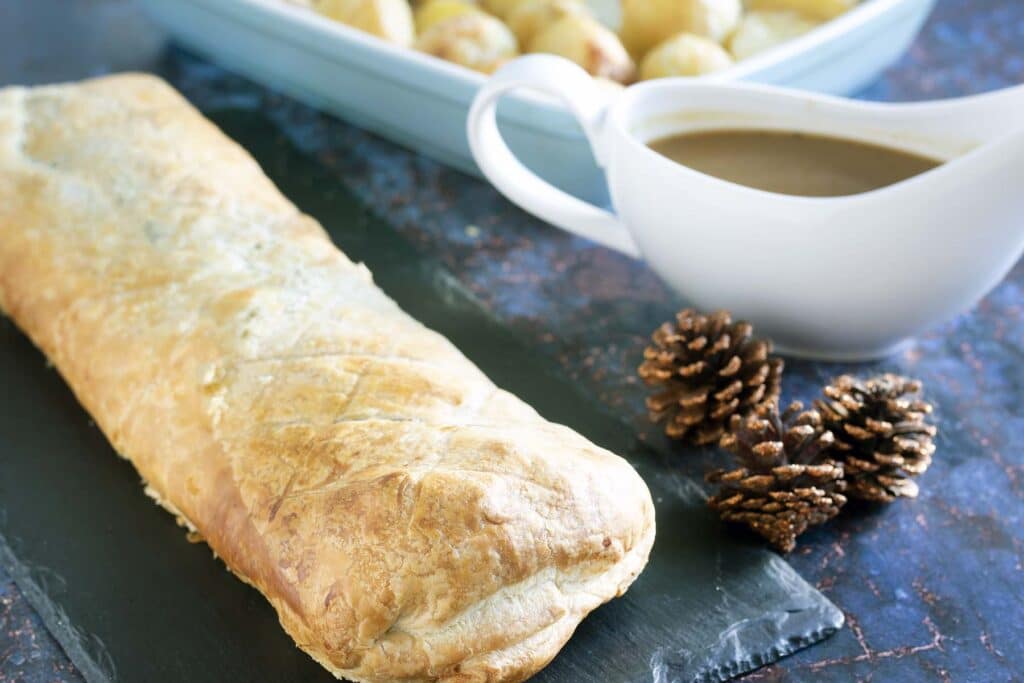 close up of vegan christmas wellington with pine cones, gravy and roast potatoes