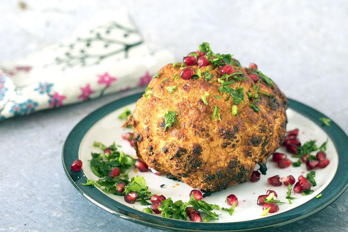 whole roasted cauliflower on plate with pomegranate seeds and herbs
