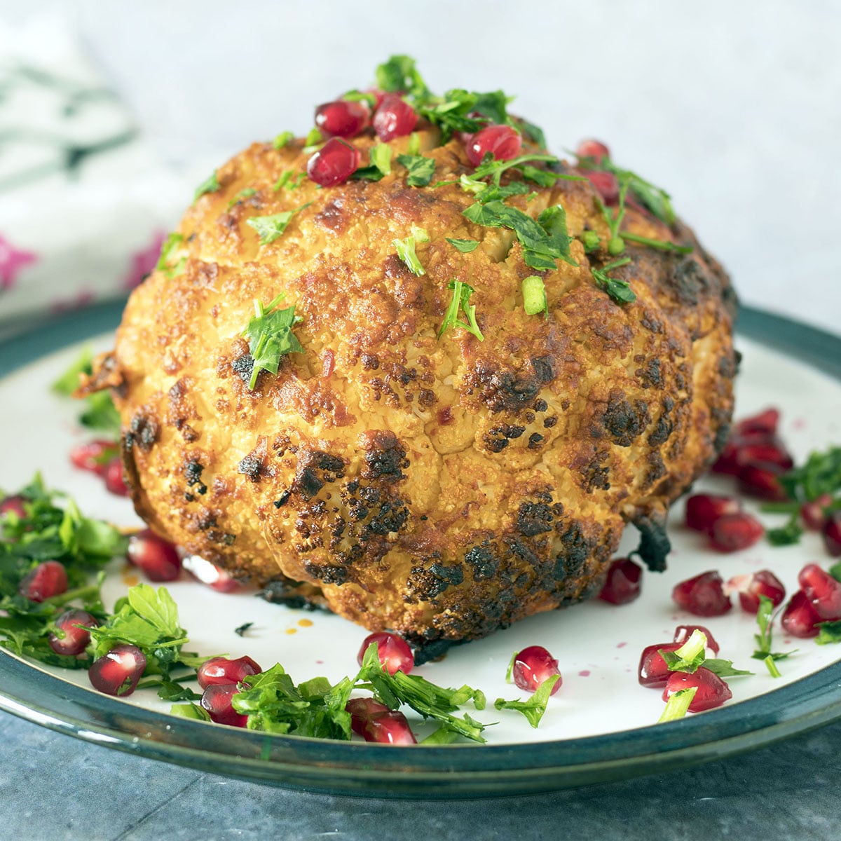 whole roasted cauliflower on plate with pomegranate seeds and herbs