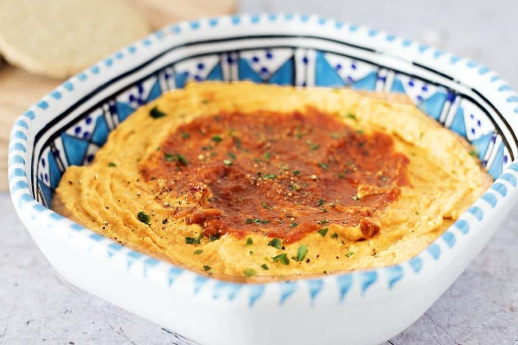 close up of harissa paste hummus dip in blue and white bowl