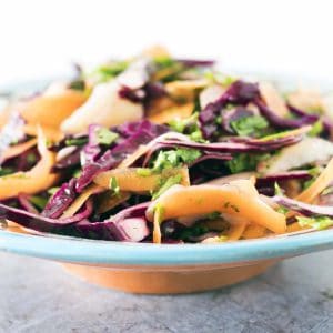 close up shot of kohlrabi, carrot and cabbage slaw in blue and white moroccan bowl