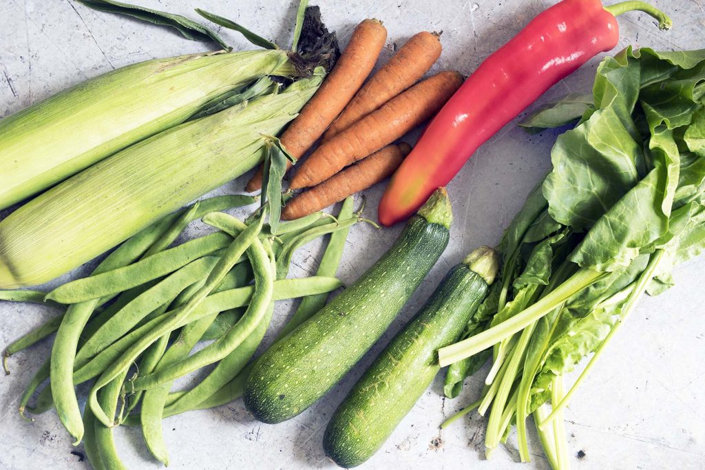 sweetcorn, carrots, red pepper, runner beans, courgette, spinach on grey background - september seasonal vegetables