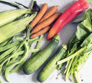 sweetcorn, carrots, red pepper, runner beans, courgette, spinach on grey background - september seasonal vegetables