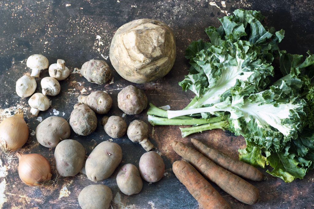 swede, kale, potatoes, carrots, jerusalem artichokes, mushrooms and onions on brown background