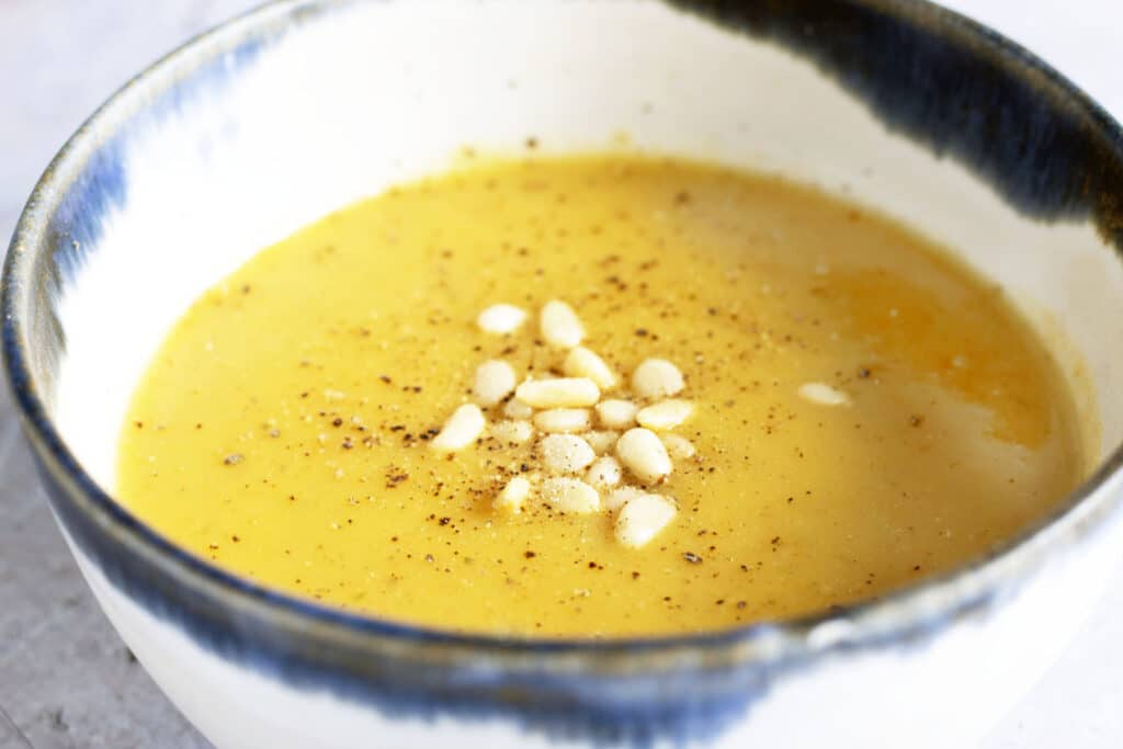 bowl of carrot and potato soup topped with pine nuts