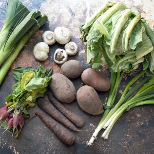 March seasonal vegetables - leeks, mushrooms, radish, cauliflower, potatoes, carrots, spring onions on brown background