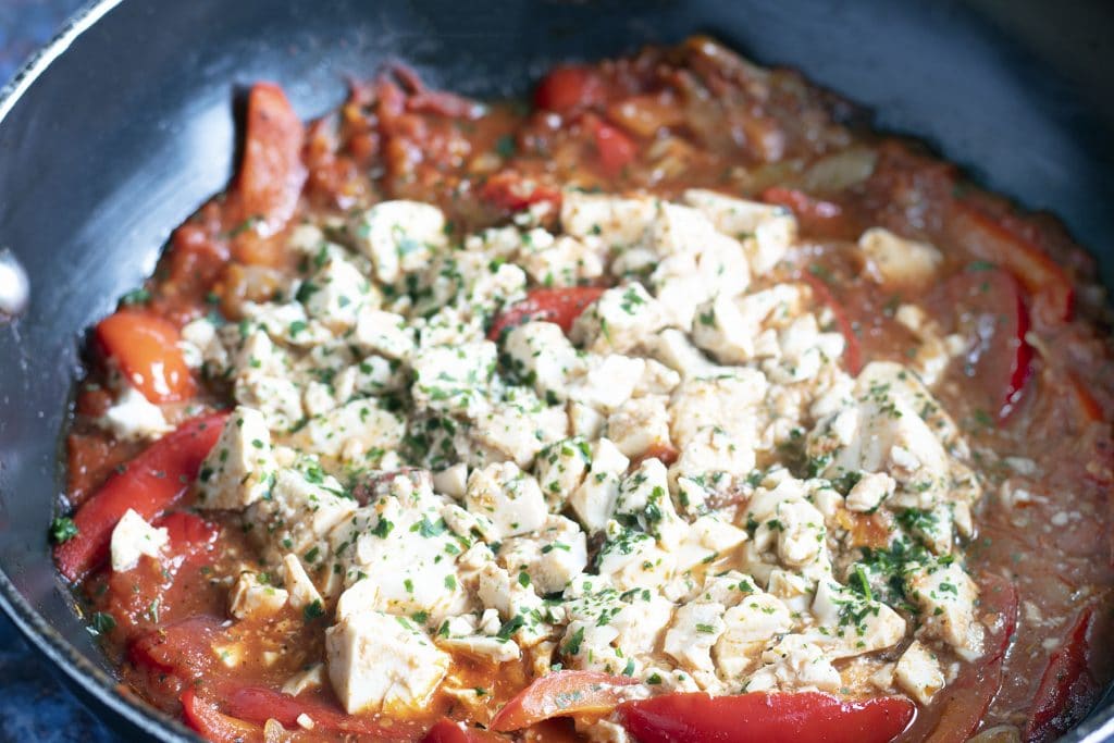 close up of red pepper and tomato shakshuka with silken tofu and herb topping