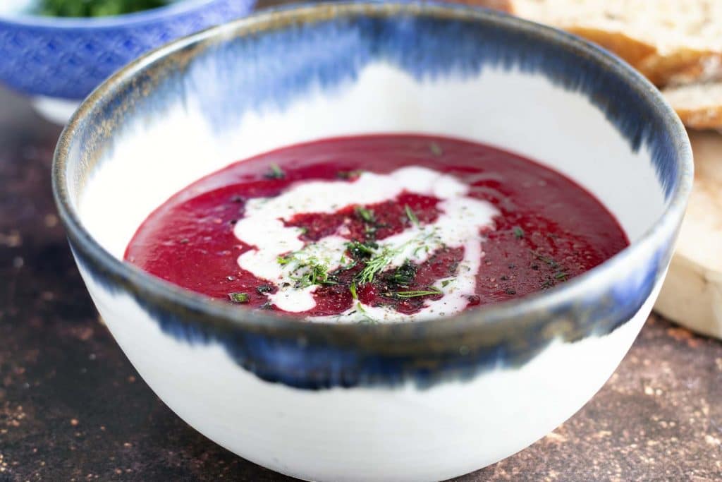 beetroot soup in blue and white bowl with bread and dill in background