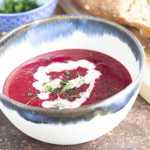 beetroot soup in blue and white bowl with bread and dill in background