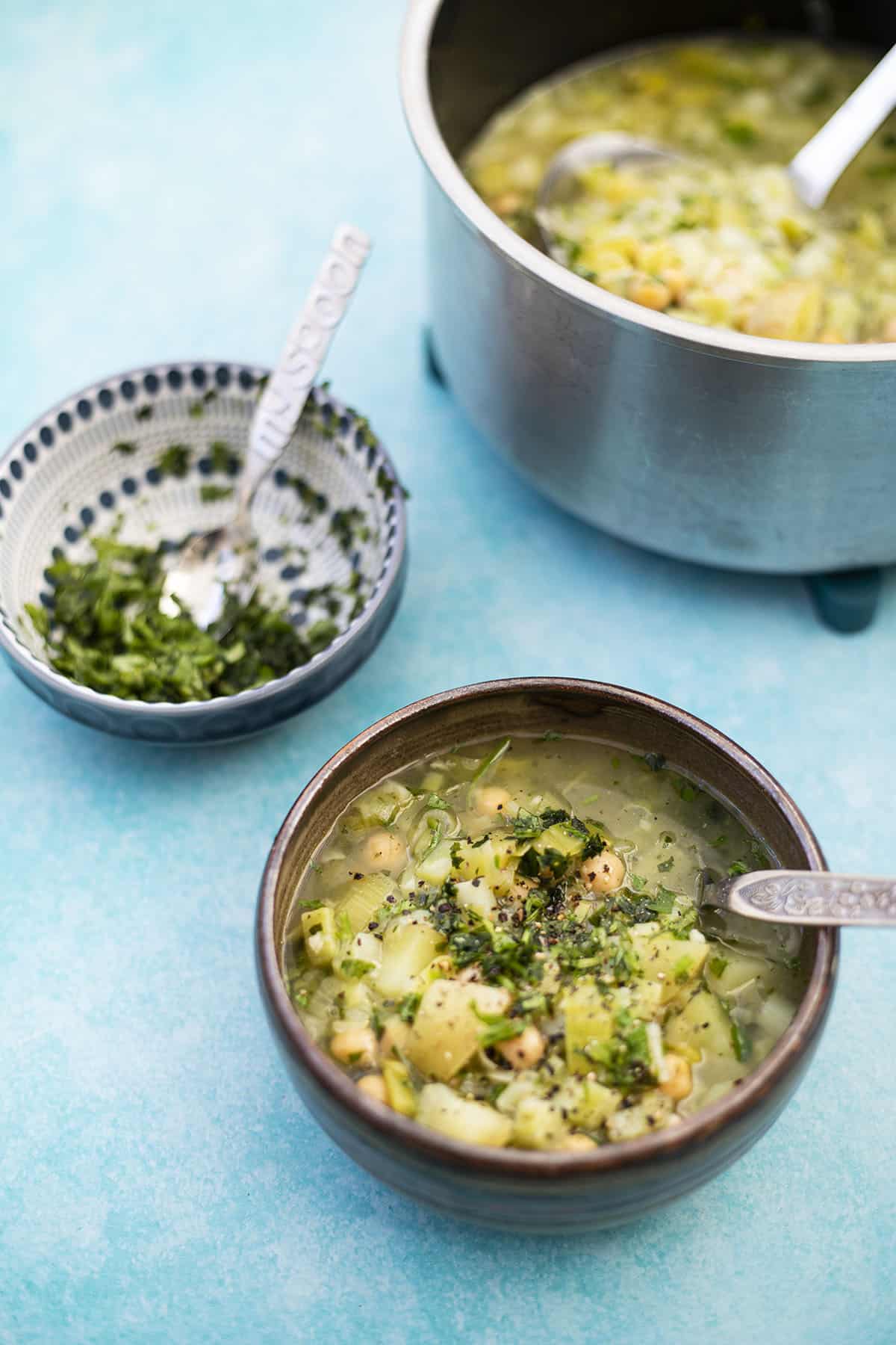 broccoli stalk soup with chickpeas and leeks in bowl with pan and bowl with herbs in background